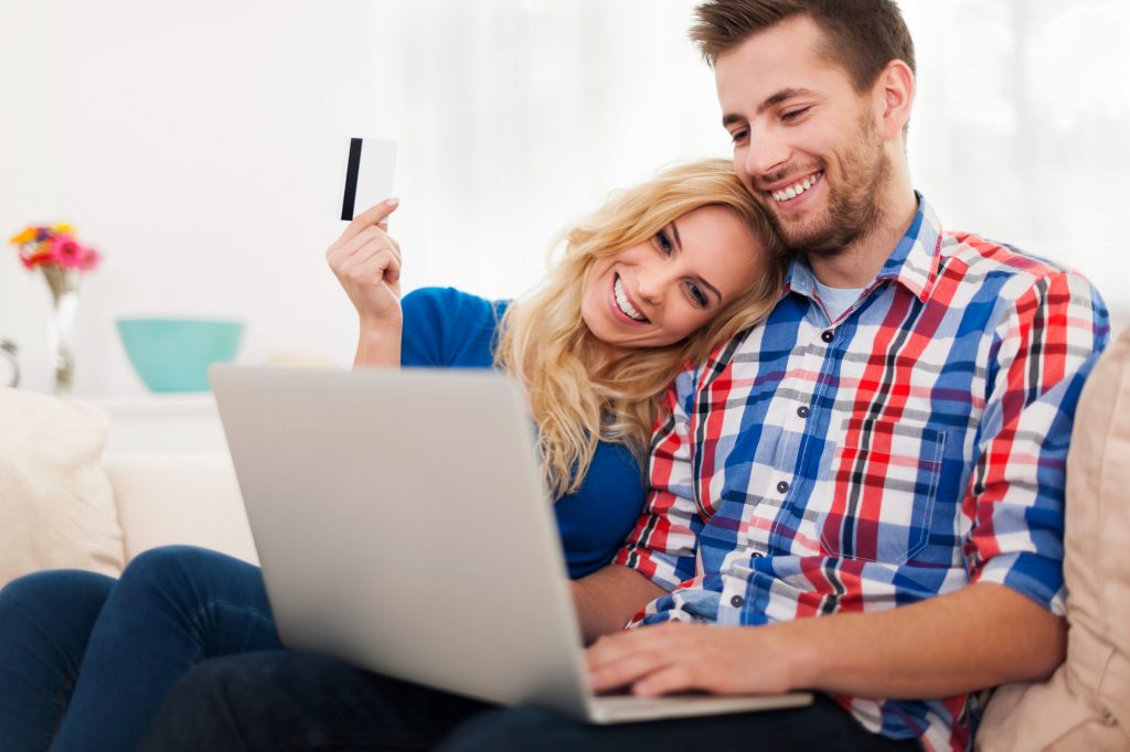Young couple sitting on a sofa paying a bill online with a credit card and laptop